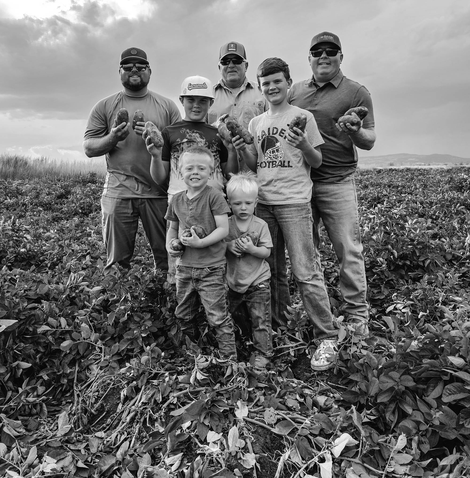 Three generations of the Baley family standing in a potato field, each holding freshly dug Russet potatoes